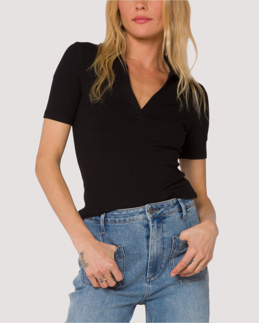 Woman wearing a black polo top and blue jeans against a white background