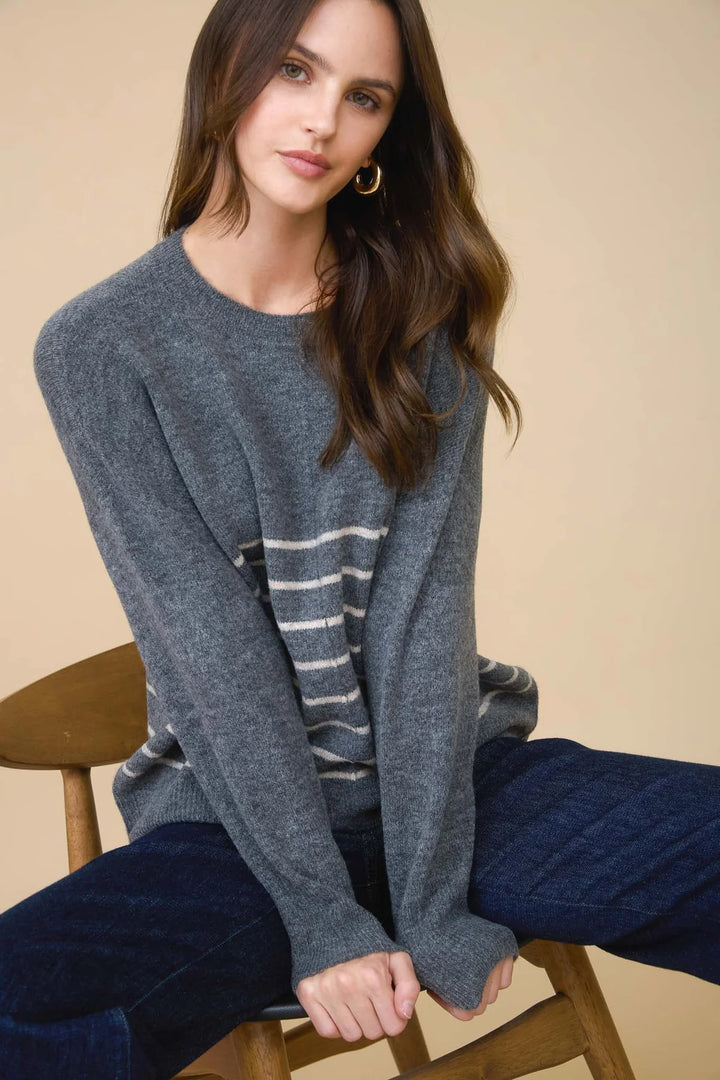 Model sitting on a chair wearing a grey sweater with white stripes on bottom half against a tan background