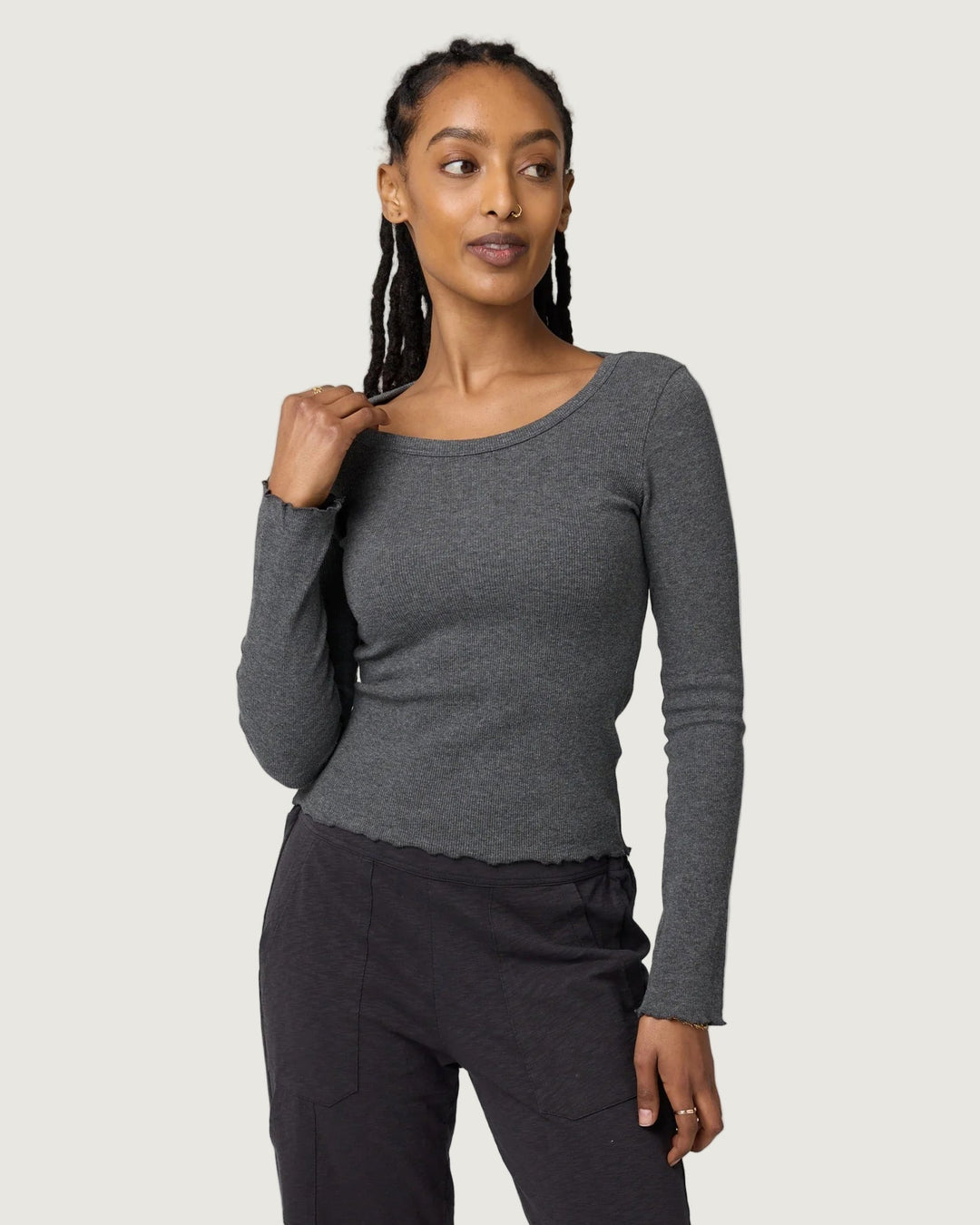 Woman wearing a gray long-sleeve top and black pants against a light gray background