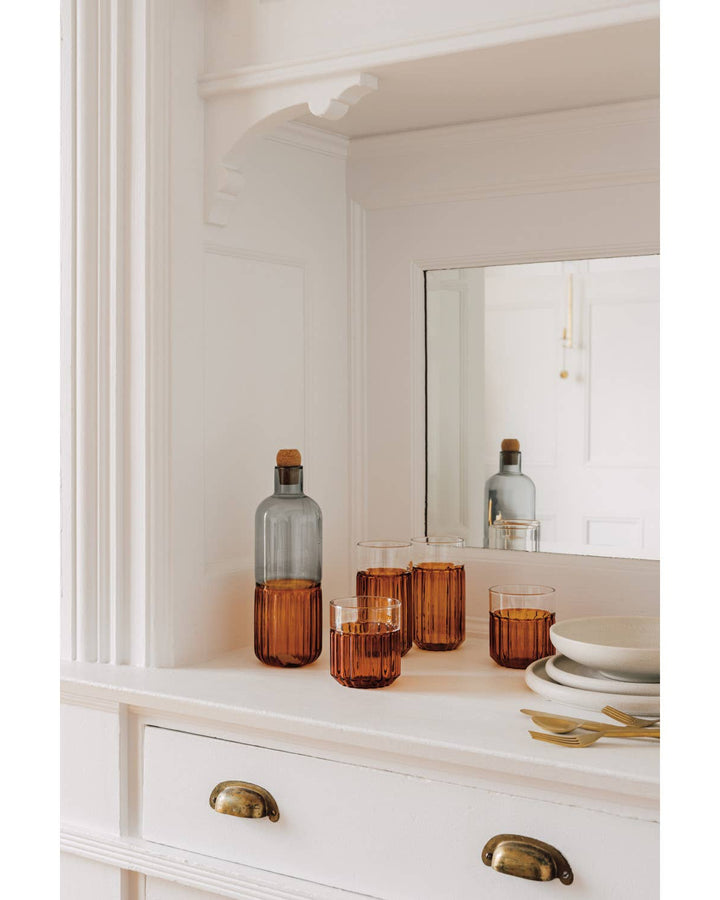 Decorative bottles and glasses on a white dresser with a mirror in the background.
