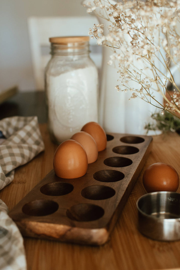 eggs in an acacia wood egg-tray with flour jar and baking supplies.
