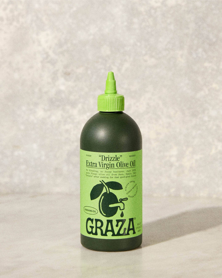 Green bottle of GRAZA olive oil on a textured white background