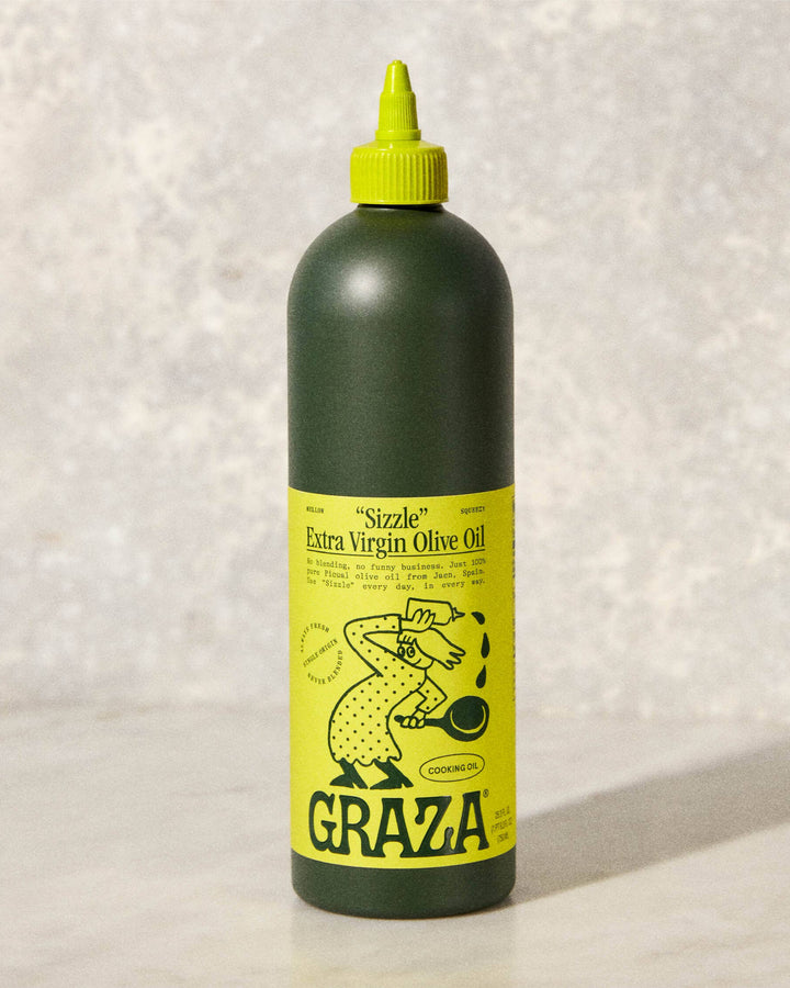 Bottle of Graza Extra Virgin Olive Oil with a yellow label on a textured white background