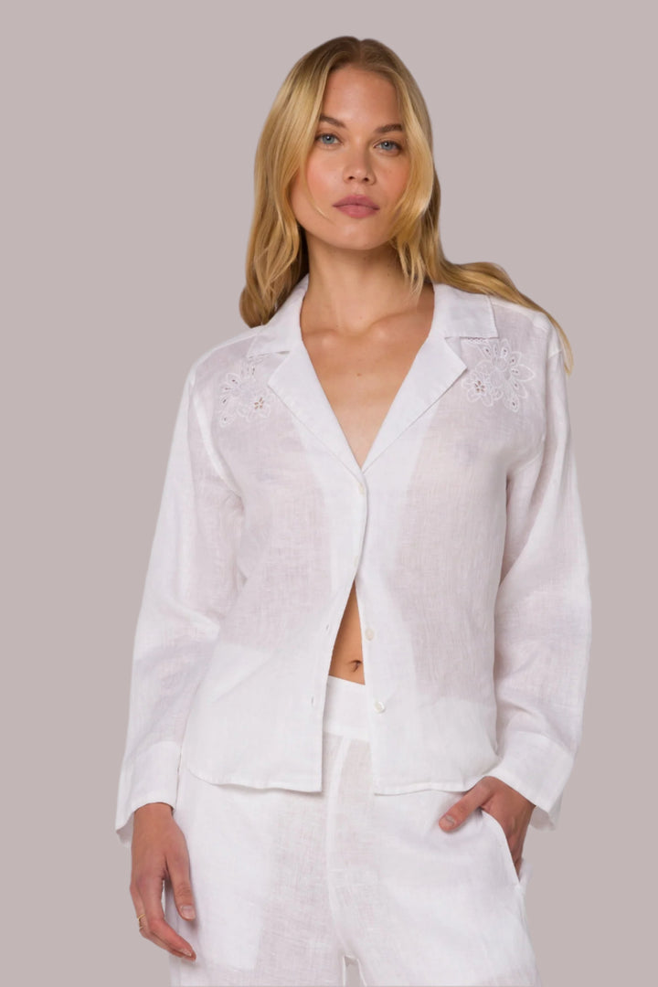 Woman wearing a white linen shirt with embroidery details against a plain background