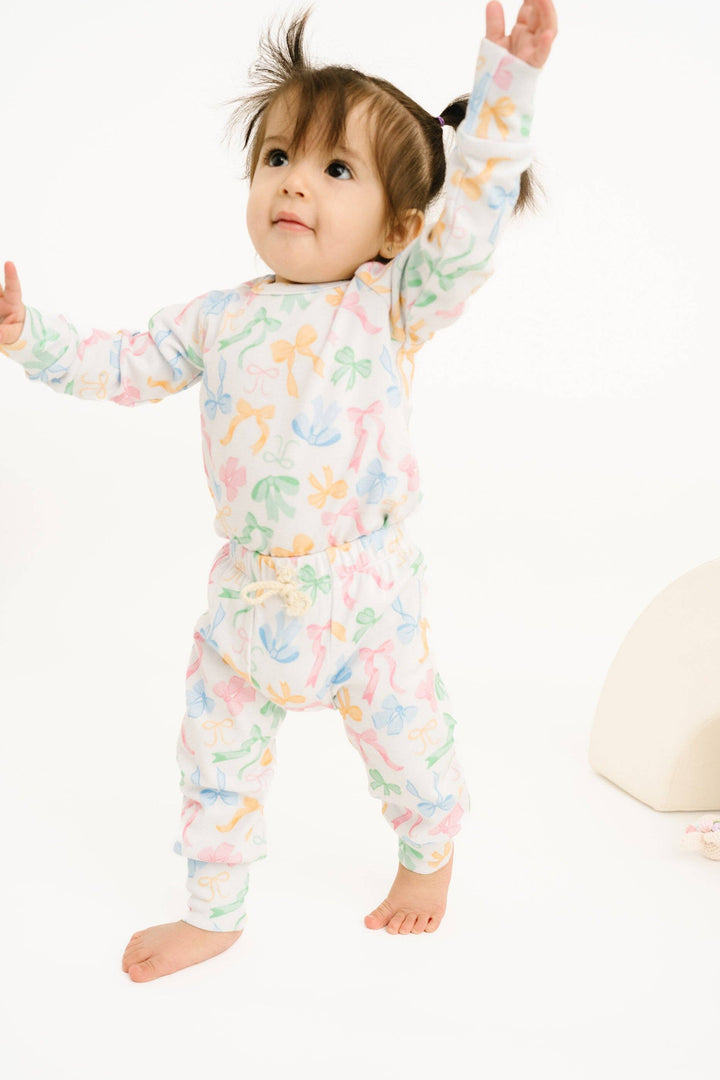 Child wearing a colorful set with long sleeves and bow print pants on a white background