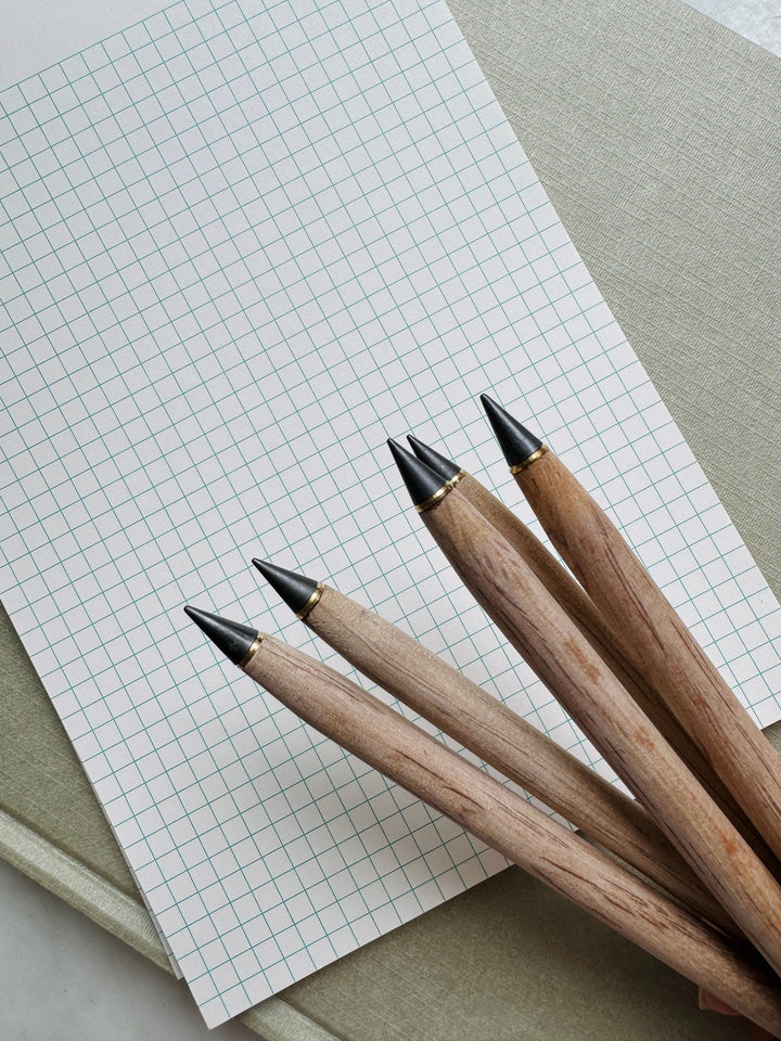 Four bamboo alloy pencils with black tips on a sheet of grid paper.
