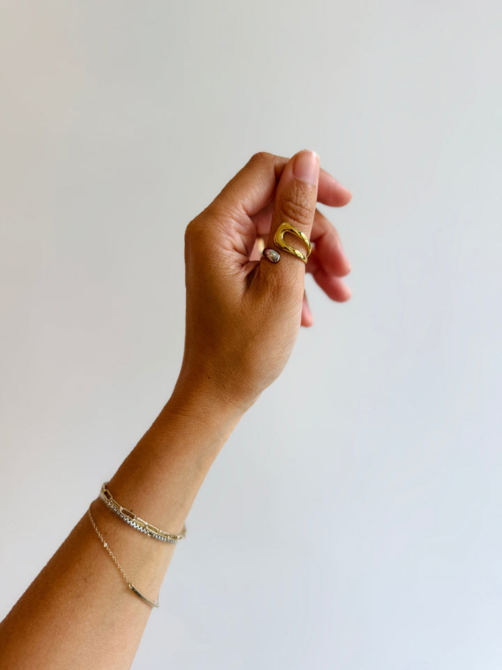 Hand wearing a gold ring and bracelet on a plain background
