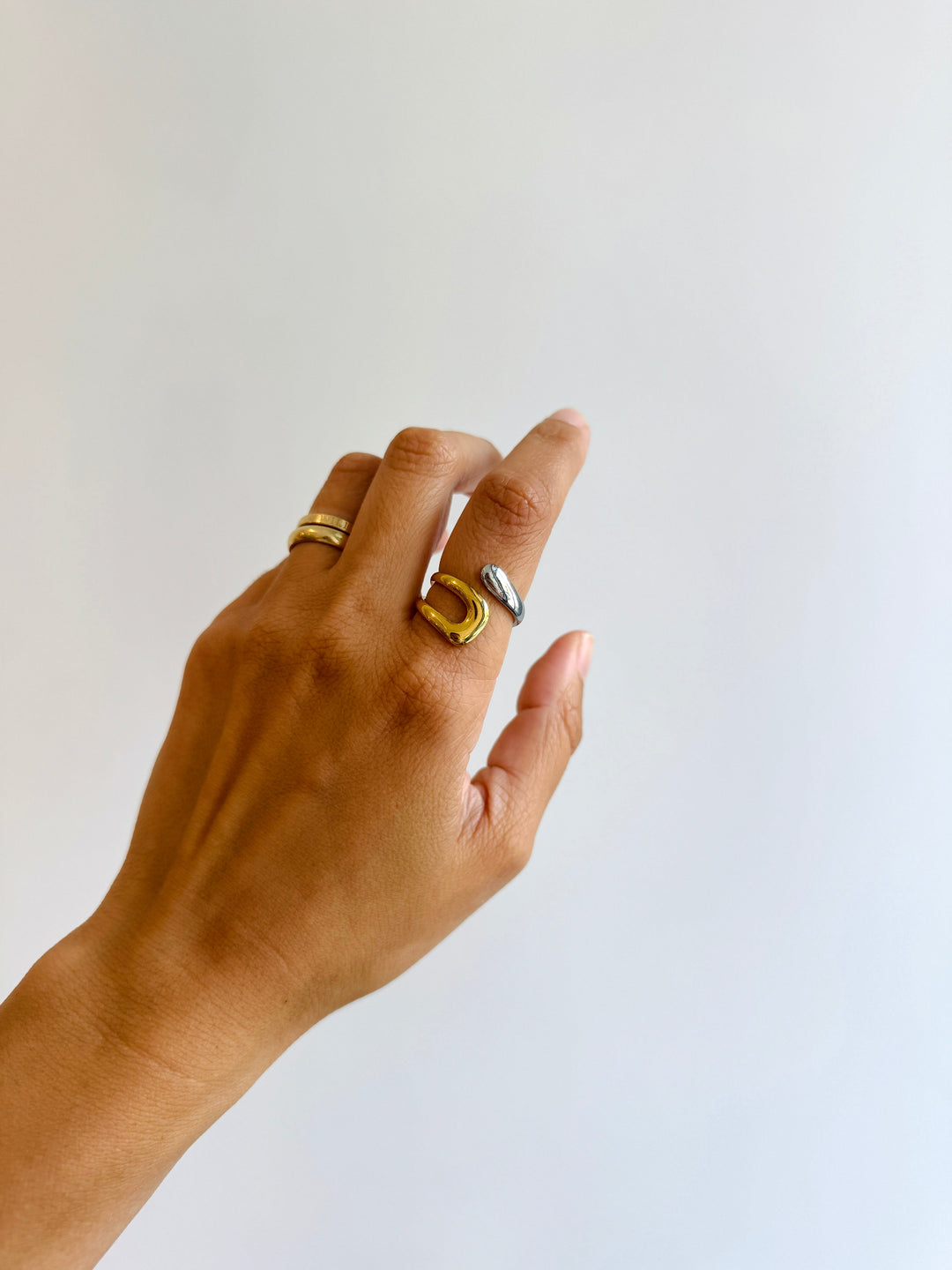 Hand wearing two gold rings on a plain background
