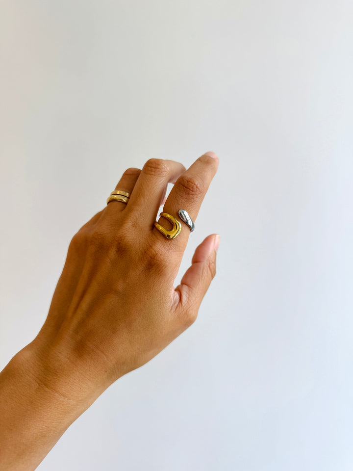 Hand wearing two gold rings on a plain background