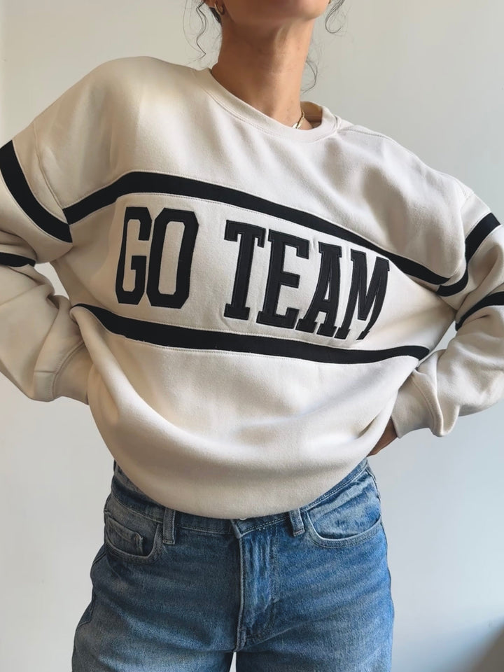 Person wearing a white sweatshirt with 'GO TEAM' text on a plain background