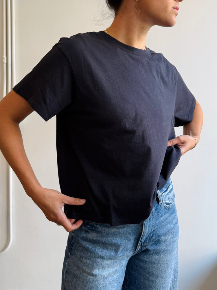 Person wearing a black t-shirt and blue jeans against a plain background