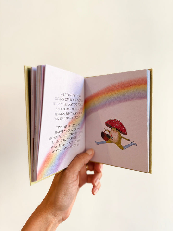 Open book with colorful illustration of a mushroom hat wearing frog and rainbow on a light background