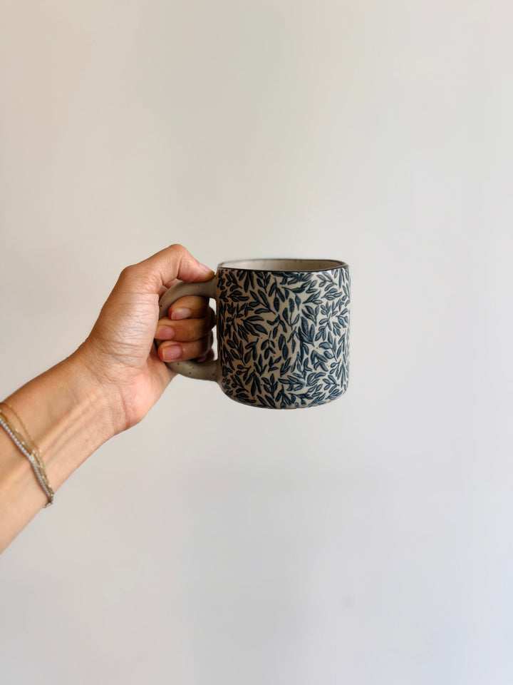 Hand holding a patterned ceramic mug against a plain background