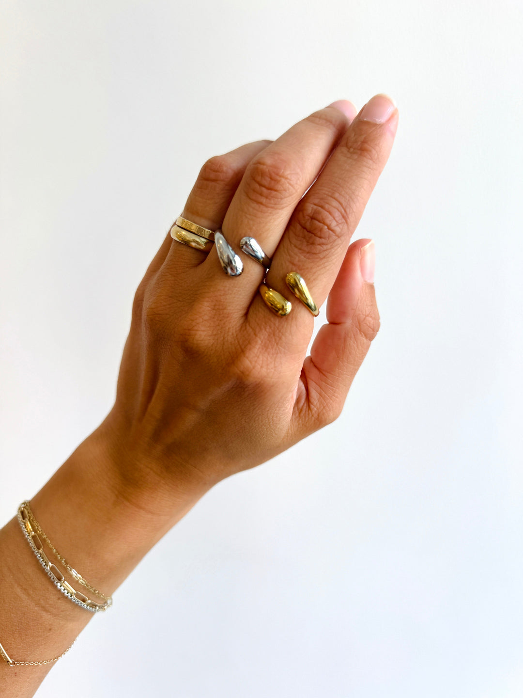 Hand wearing multiple gold and silver rings on a white background