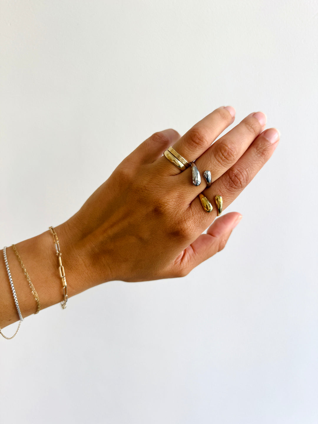 Hand wearing multiple gold rings and bracelets on a white background