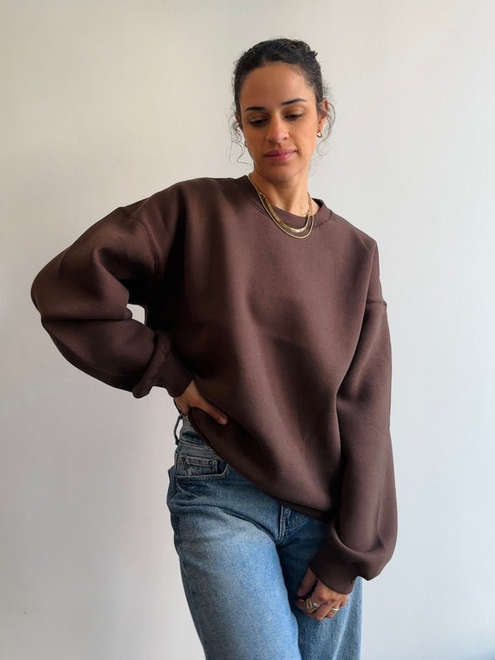 Person wearing a brown sweatshirt and blue jeans against a plain background