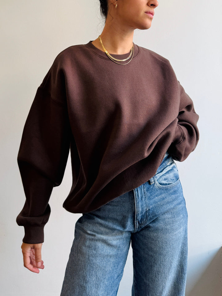 Person wearing a brown sweatshirt and blue jeans against a plain background