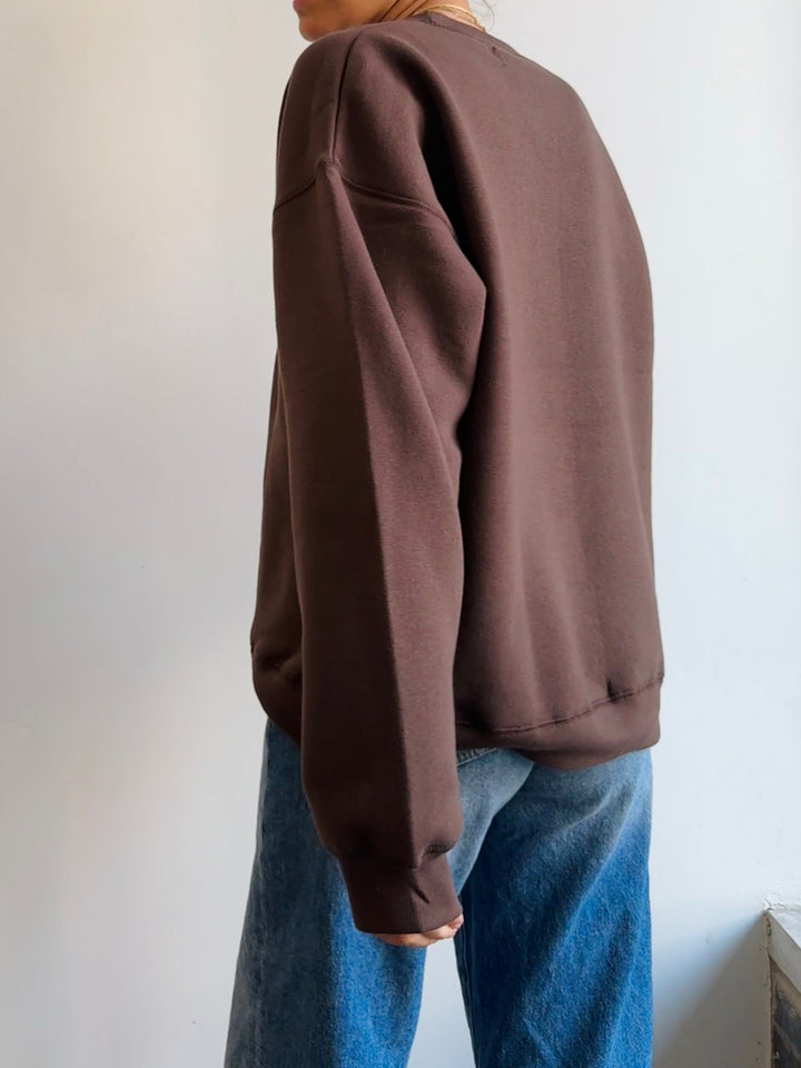 Person wearing a brown sweatshirt and blue jeans against a plain background
