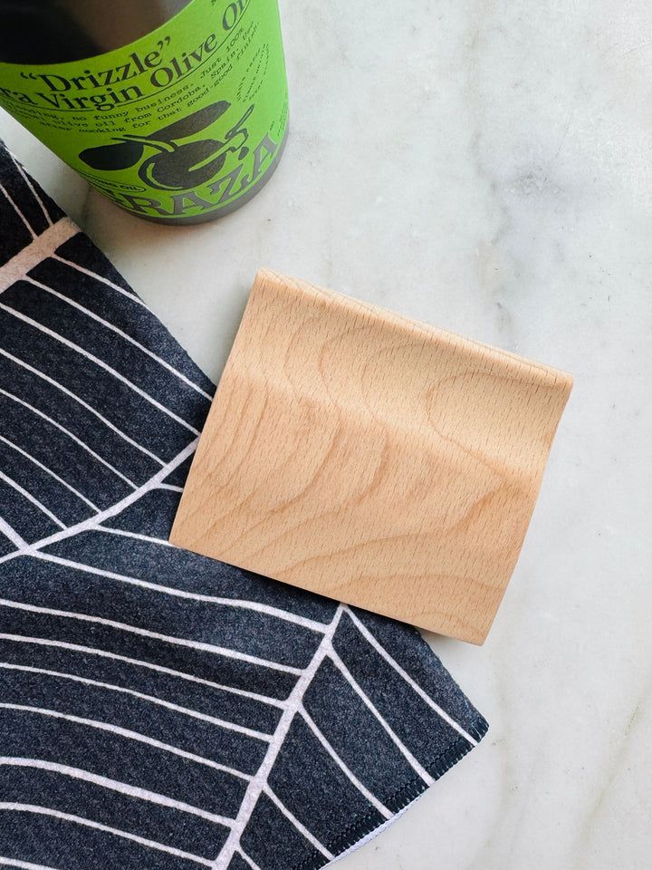 Wooden scraper and kids knife on a marble surface with a bottle of olive oil in the background