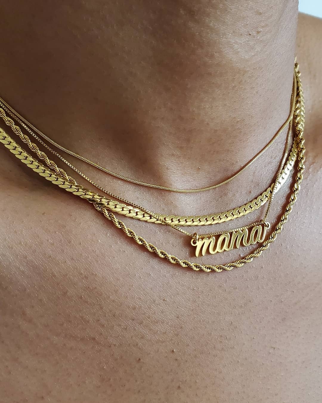 Gold necklaces on a person's neck with 'mama' pendant