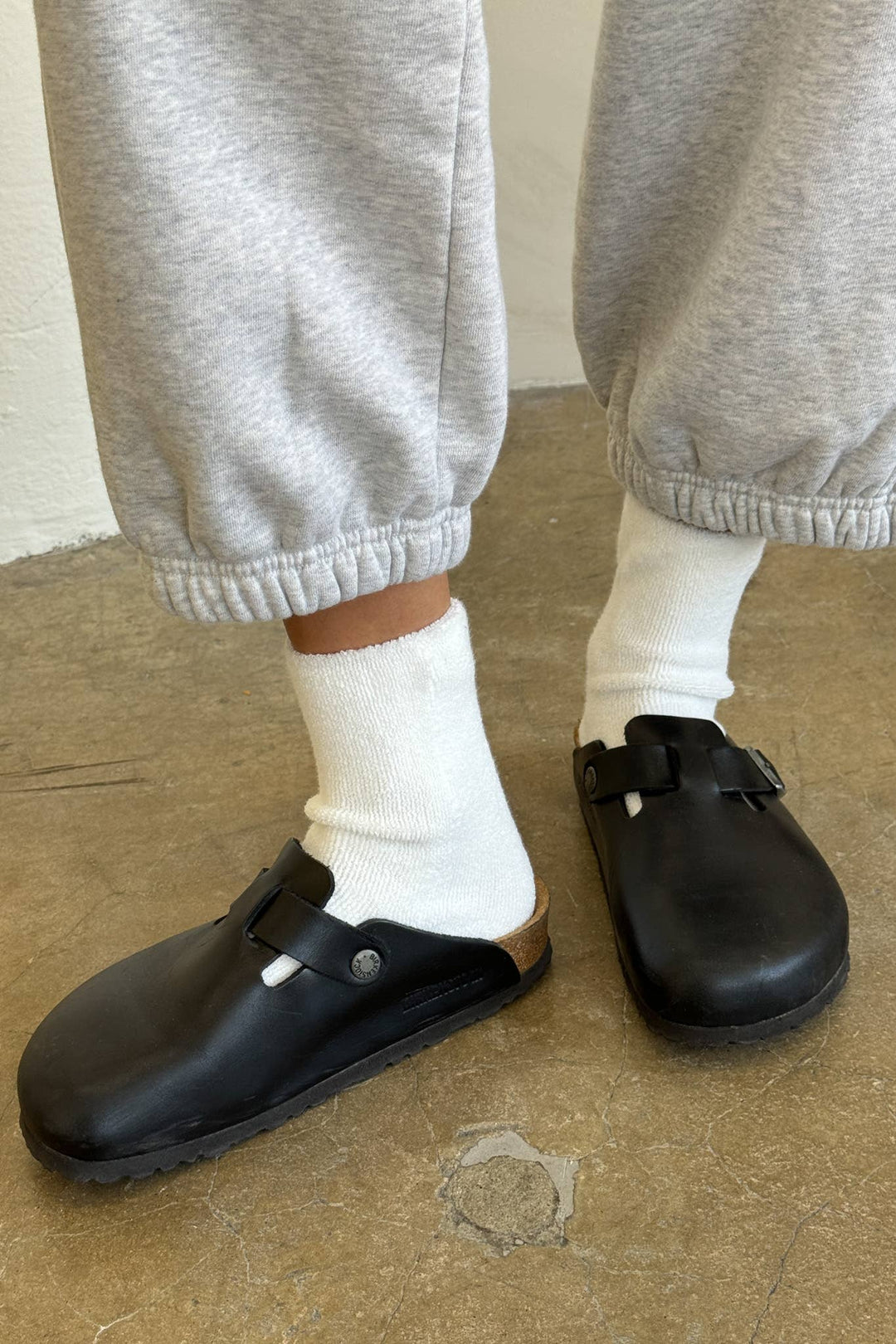 Person wearing black clogs, white socks, and gray sweatpants on a beige floor.