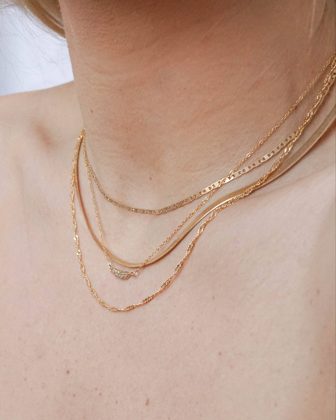 Close-up of a person wearing two gold necklaces on a plain background