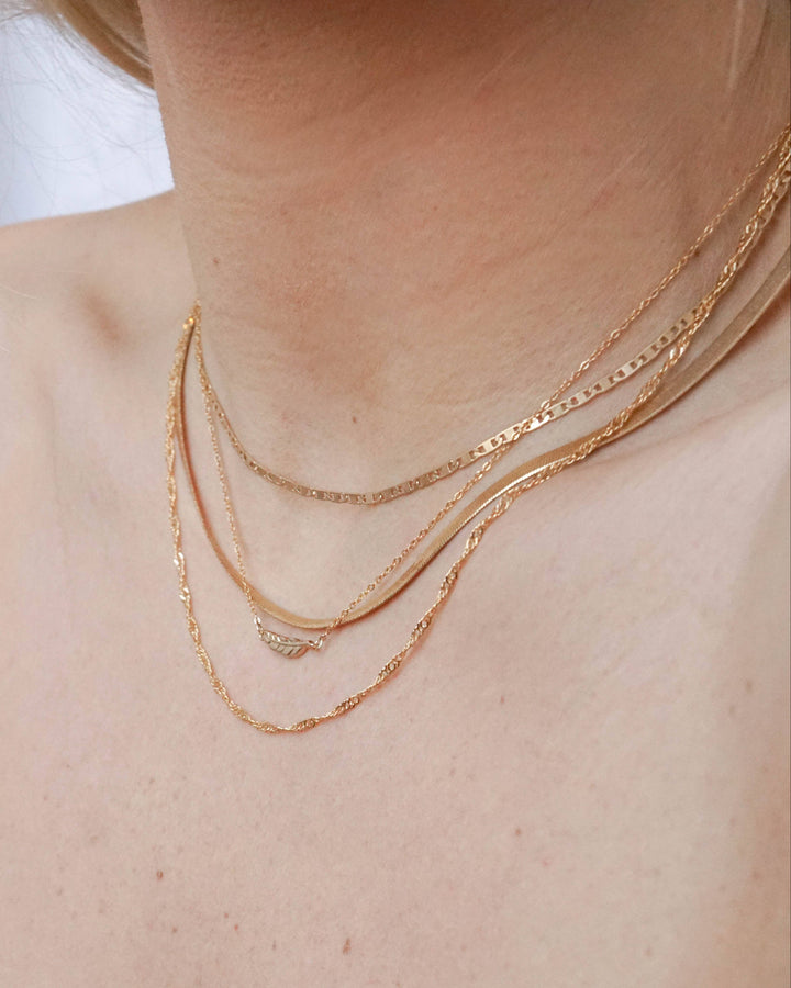 Close-up of a person wearing two gold necklaces on a plain background