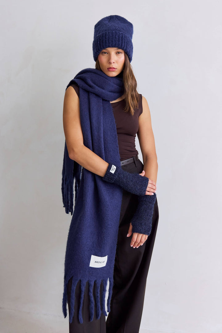 Woman wearing a navy blue scarf, beanie, and gloves on a plain background