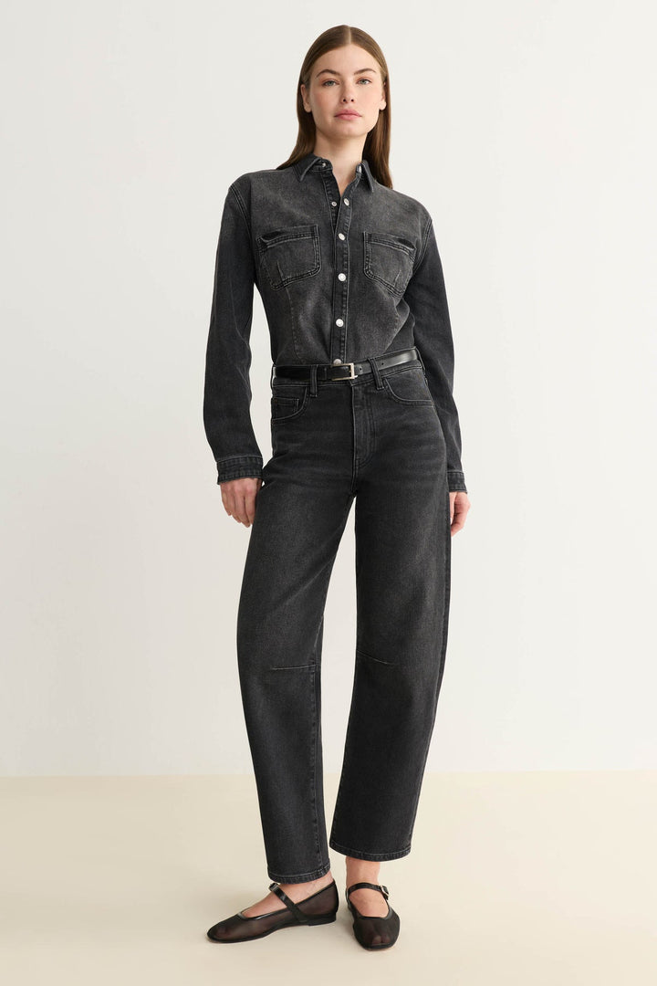 Woman wearing a black denim shirt and barrel leg jeans on a white background