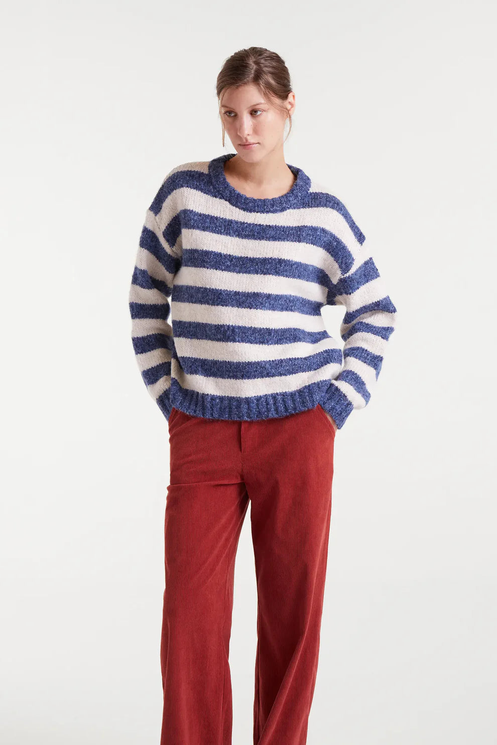 Person wearing a blue and white striped sweater with red pants on a white background