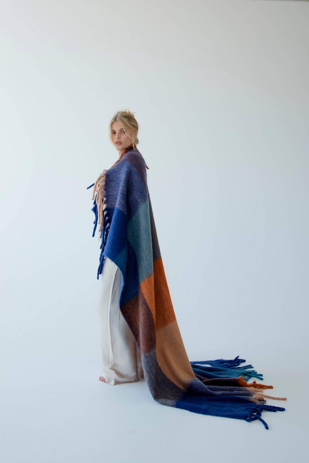 Person wearing a colorful blanket draped over their shoulders against a white background