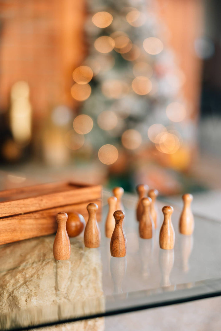 Wooden figurines on a reflective surface with a blurred festive background