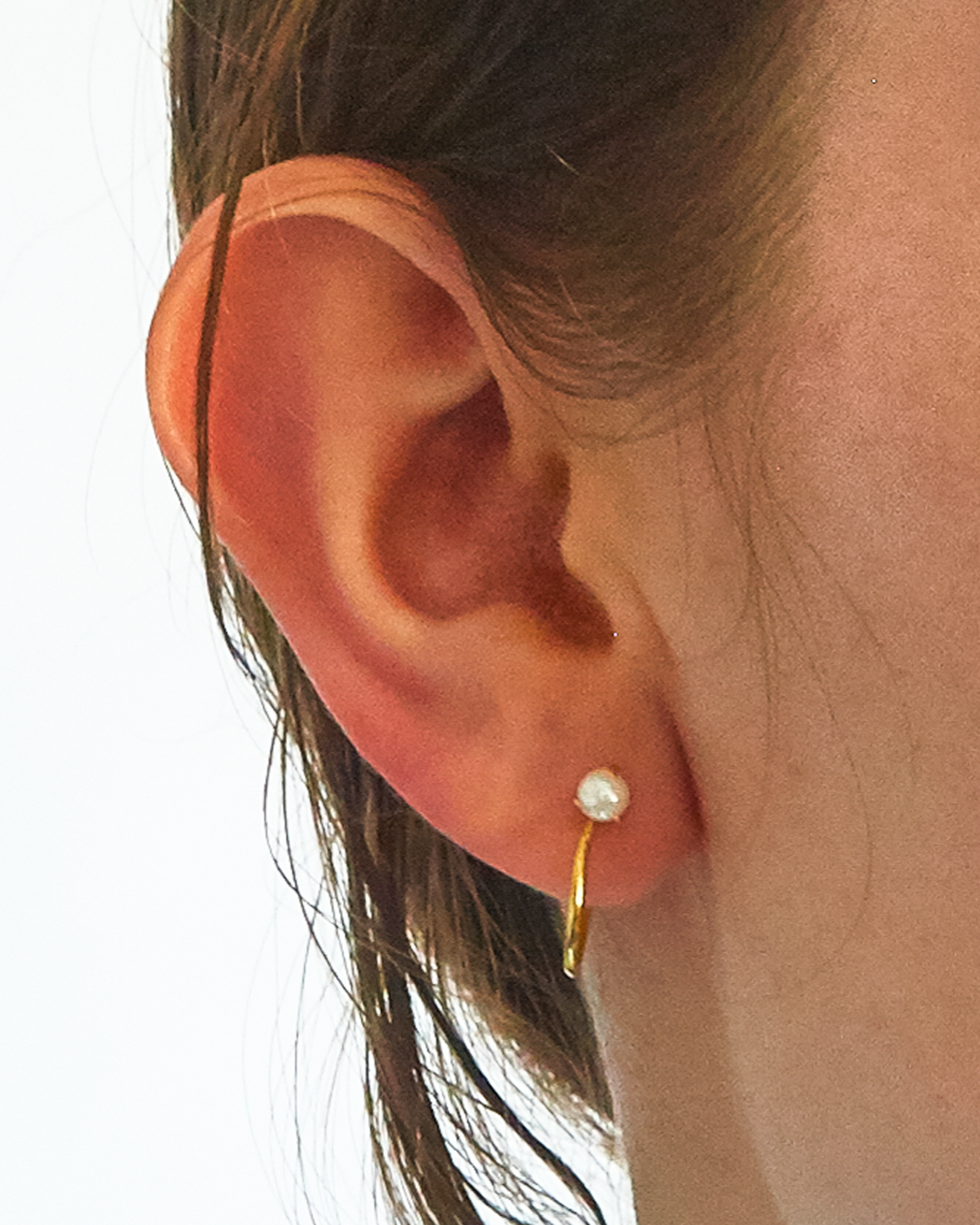 Close-up of an ear wearing a gold hoop earring with a pearl center.