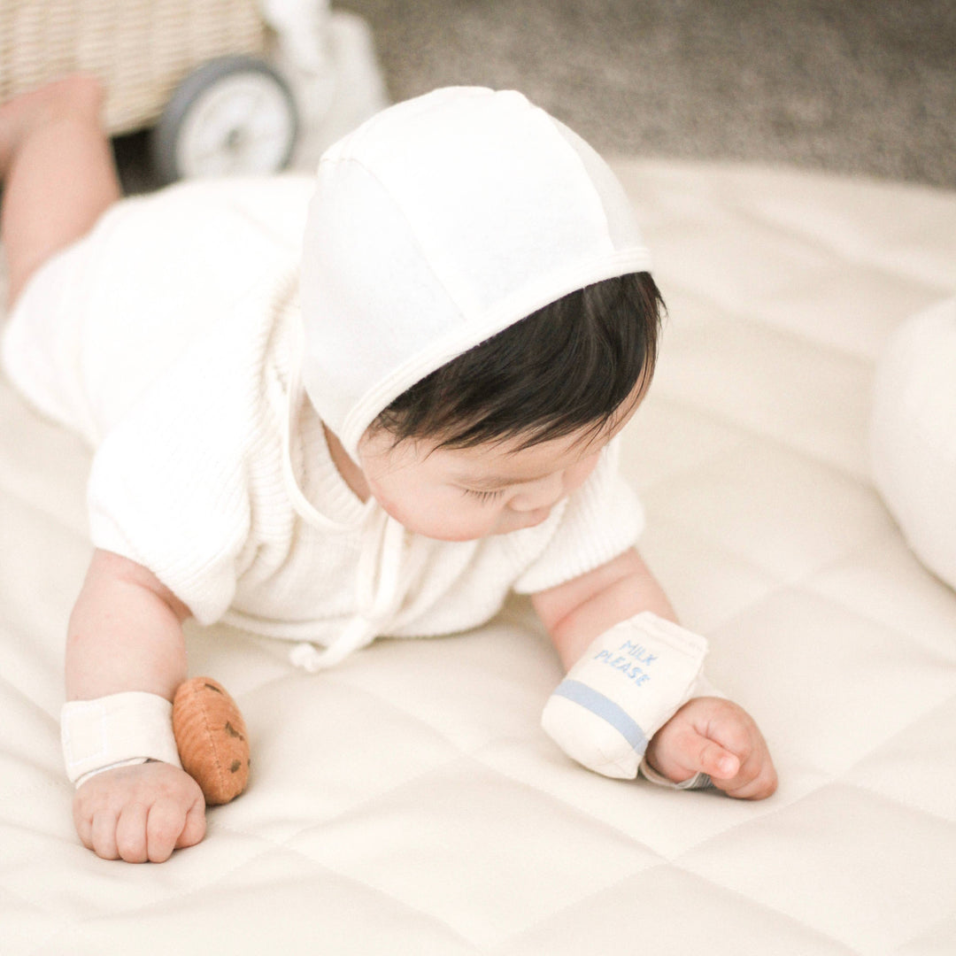 Baby in white outfit with a toy on a light surface