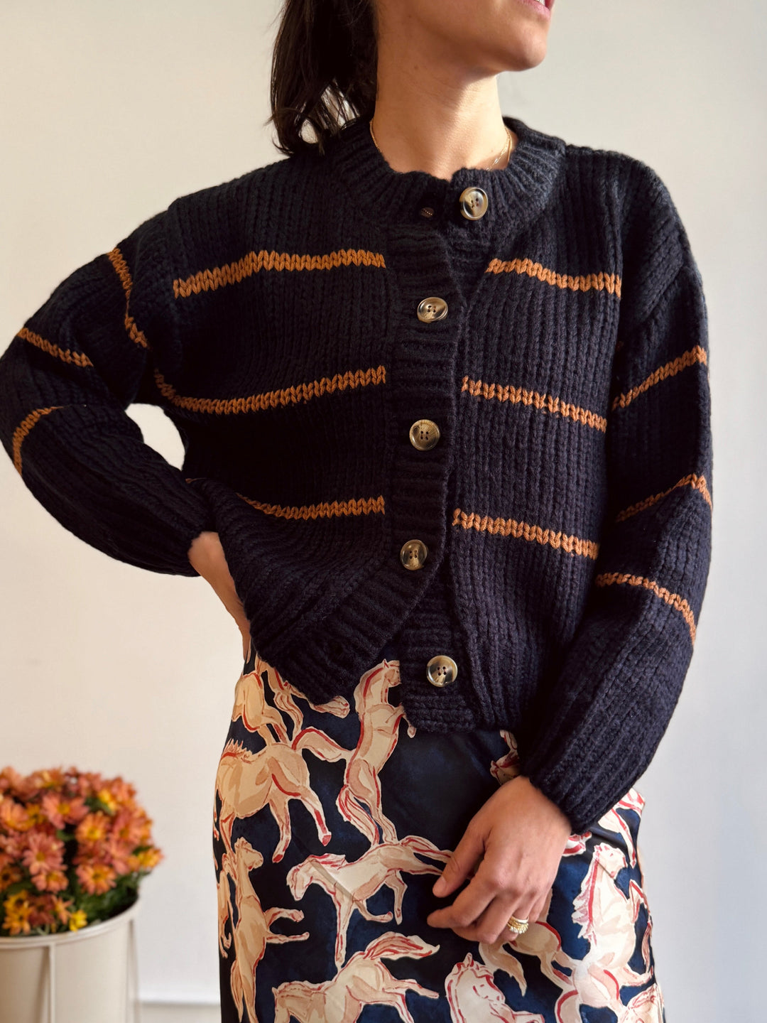 Person wearing a dark blue cardigan with gold stripes, standing against a neutral background.