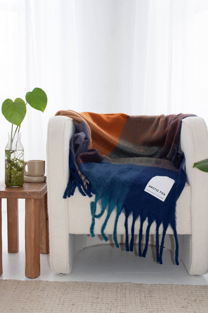 Colorful blanket draped over a white chair in a room with a wooden side table and plants.