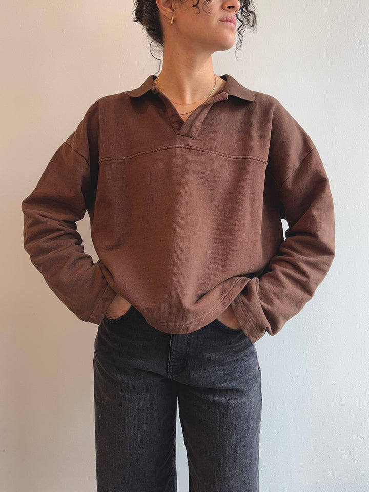 Person wearing a brown pullover with a collar against a neutral background