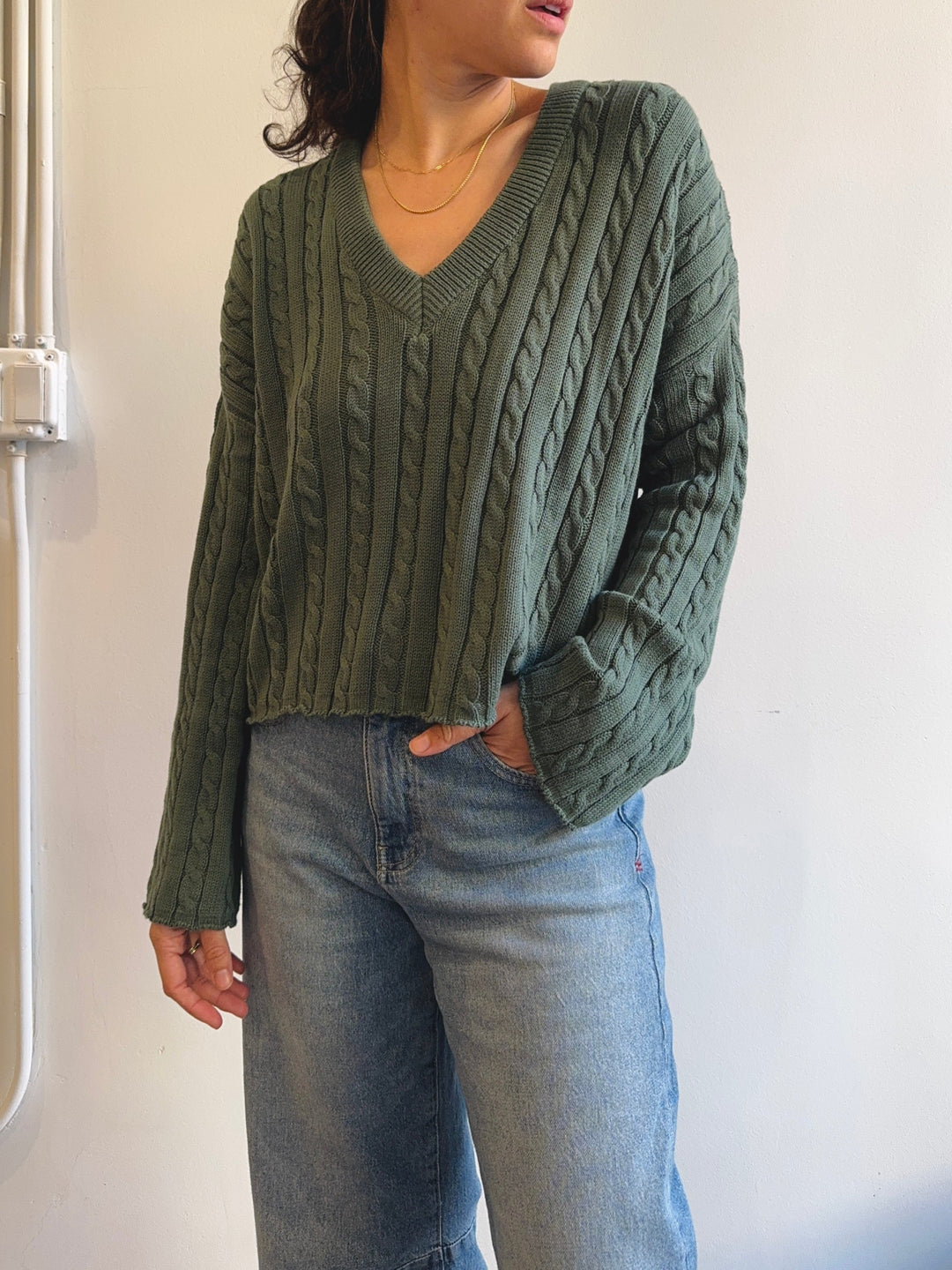 Person wearing a green cable knit sweater and blue jeans against a white background