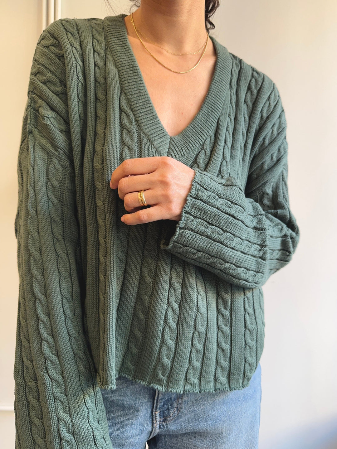 Person wearing a green cable knit sweater with a neutral background