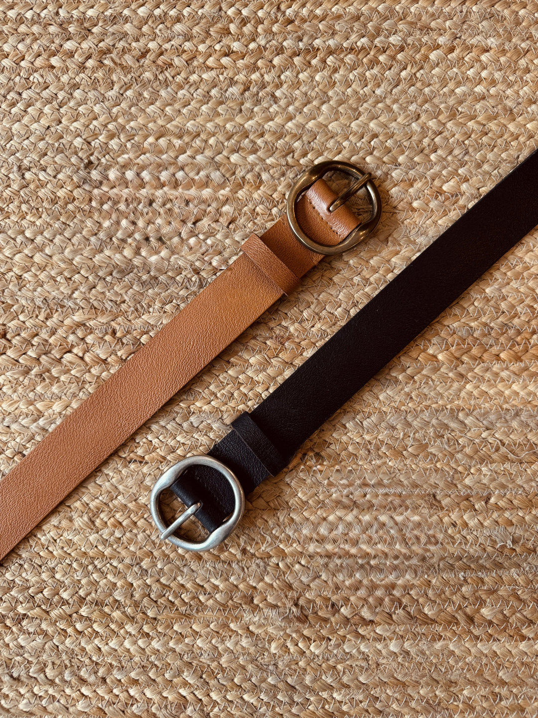 Two belts, one brown and one black, on a textured beige surface.