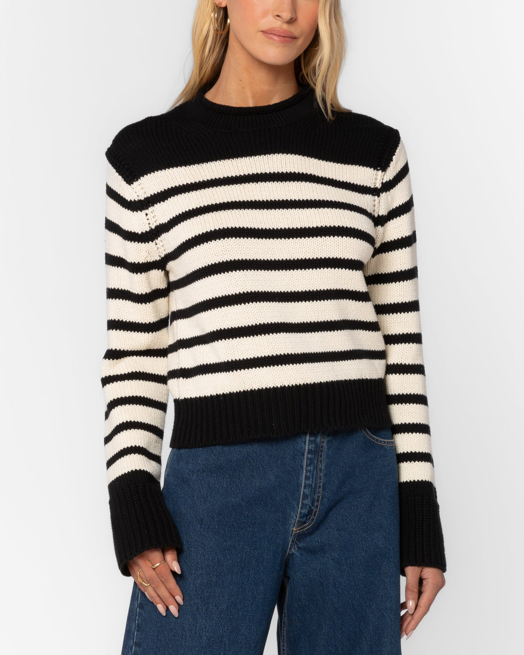 Woman wearing a black and white striped sweater with blue jeans on a white background