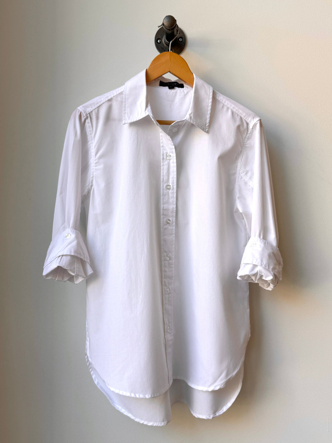 White shirt on a wooden hanger against a plain wall