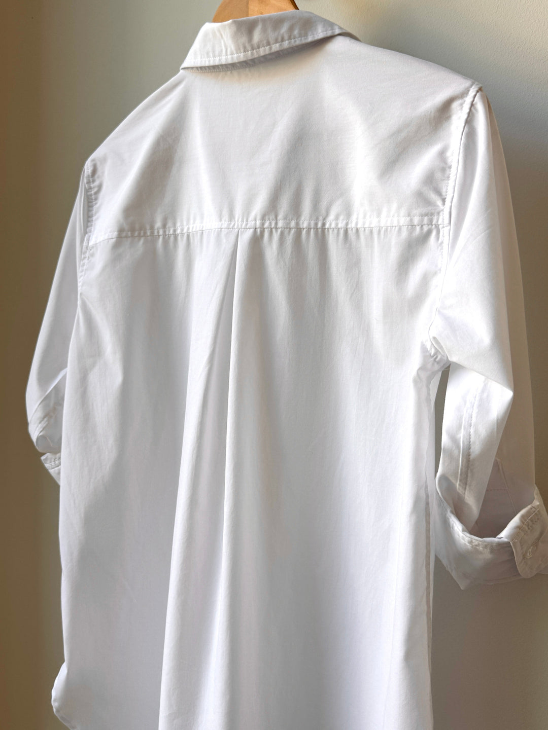 White shirt on a wooden hanger against a plain background