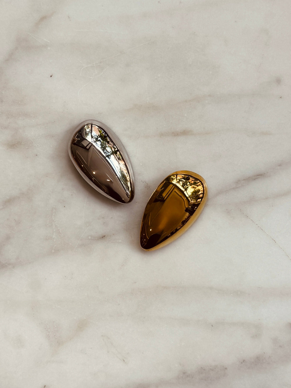 A gold and silver tear drop shaped pin on brooch against a marble surface.