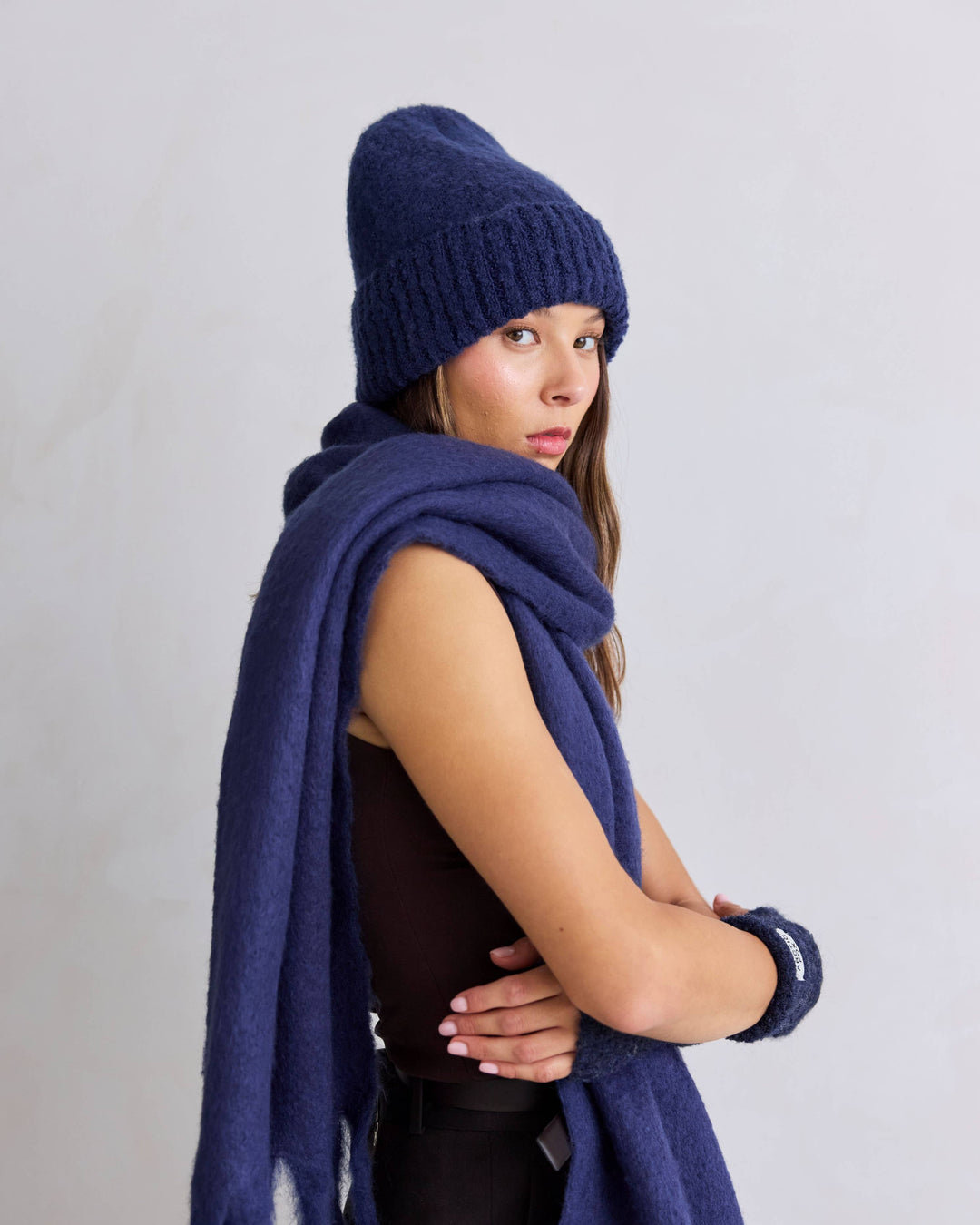 Woman wearing a blue knit beanie and scarf against a light gray background