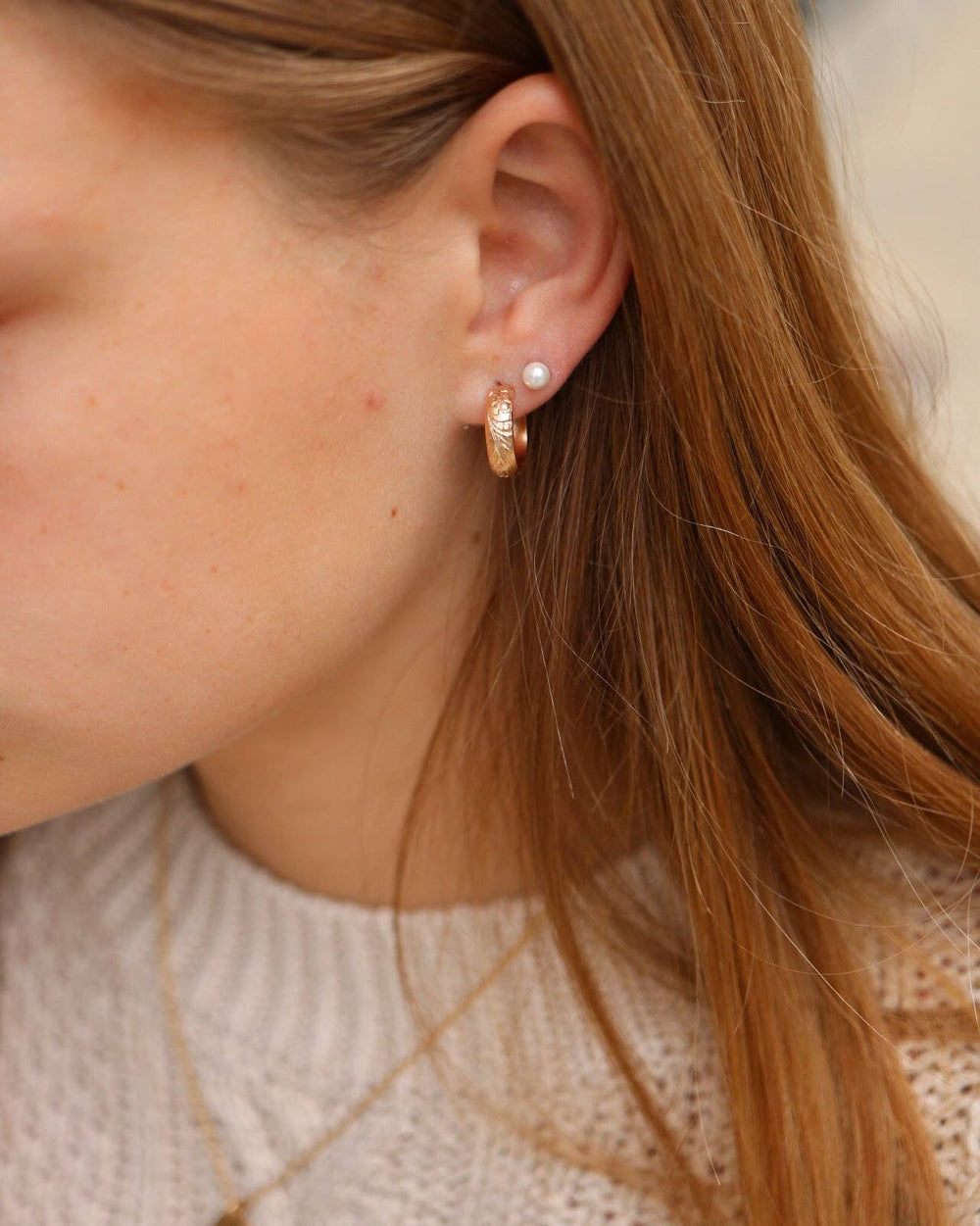 Close-up of a person wearing gold hoop earrings and a necklace.