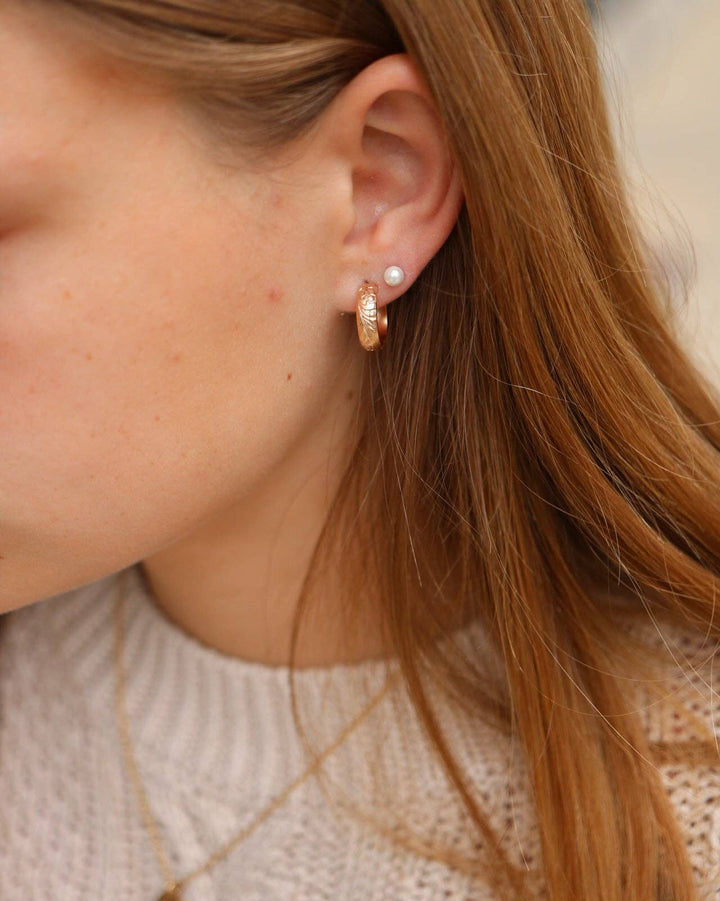 Close-up of a person wearing gold hoop earrings and a necklace.