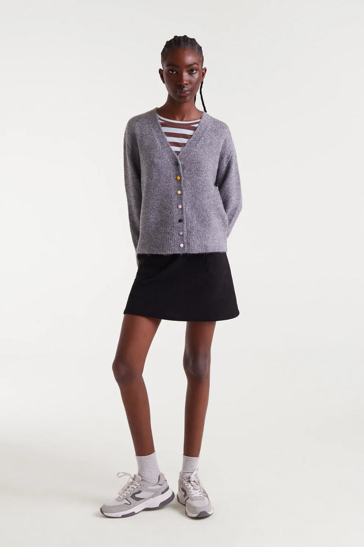 Person wearing a gray cardigan, black skirt, and striped shirt on a white background