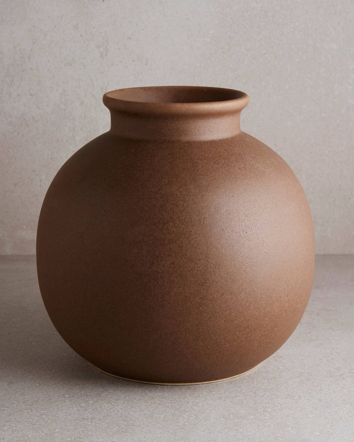a round ceramic flower vase with a small lip at the opening in matte brown glaze