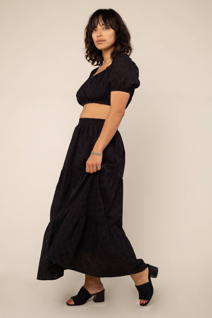 Woman wearing a black outfit with a tiered midi skirt and top on a beige background